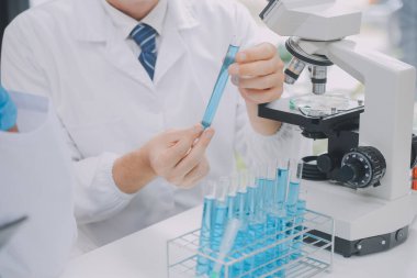 Biyoteknoloji laboratuvarında çalışan bilim adamı veya laboratuvar önlüğü, araştırma için mikroskop ekipmanı ve klinik laboratuarında cam şişede karıştırıcı reaktörler..