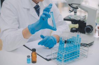 Biyoteknoloji laboratuvarında çalışan bilim adamı veya laboratuvar önlüğü, araştırma için mikroskop ekipmanı ve klinik laboratuarında cam şişede karıştırıcı reaktörler..