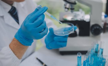 Biyoteknoloji laboratuvarında çalışan bilim adamı veya laboratuvar önlüğü, araştırma için mikroskop ekipmanı ve klinik laboratuarında cam şişede karıştırıcı reaktörler..