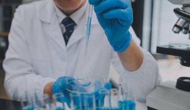 Biyoteknoloji laboratuvarında çalışan bilim adamı veya laboratuvar önlüğü, araştırma için mikroskop ekipmanı ve klinik laboratuarında cam şişede karıştırıcı reaktörler..