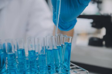 Biyoteknoloji laboratuvarında çalışan bilim adamı veya laboratuvar önlüğü, araştırma için mikroskop ekipmanı ve klinik laboratuarında cam şişede karıştırıcı reaktörler..