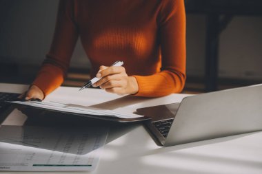 Asyalı iş kadını dizüstü bilgisayar kullanıyor ve ofiste hesap makinesi ile çalışıyor, mali raporu, iş planı yatırımını, mali analiz konseptini analiz etmeyi planlıyor..