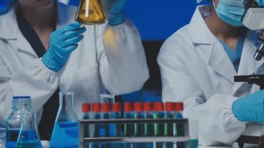 Mikroskop ve test tüpleriyle koruyucu eldivenler ve eldivenlerle laboratuvar çalışanı.