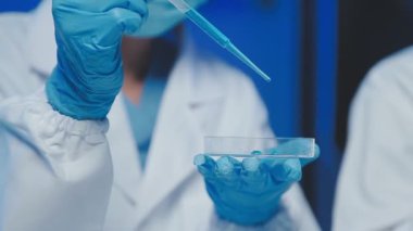 Laboratuvarda sıvı testi yapan koruyucu eldivenli bilim adamlarının görüntüsünü kapat..
