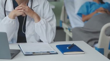 Beyaz önlüklü genç bir doktor ve hastane masasında oturuyor.