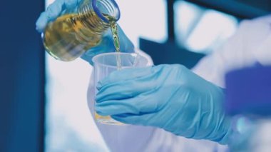 Mavi koruyucu gözlüklü laboratuvar asistanı kimyasal analiz için bir test tüpü tutuyor.