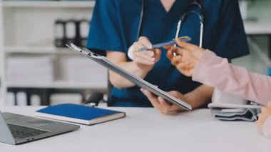 Beyaz önlüklü ve mavi üniformalı genç doktor hastane ofisinde dijital tablet tutuyor.