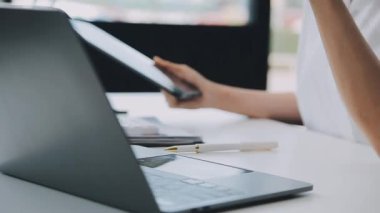 Ofiste dizüstü bilgisayar ve tablet kullanan genç bir kadın.