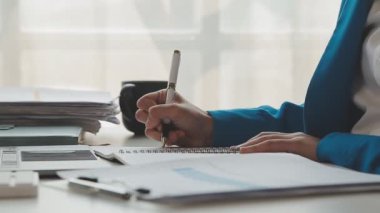 İş kadını deftere yazı yazıyor ve masadaki belgelerle çalışıyor..