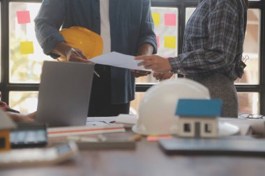 A team of construction engineers talks to managers and construction workers at the construction site. Quality inspection, work plan, home and industrial building design project