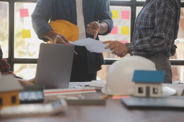 A team of construction engineers talks to managers and construction workers at the construction site. Quality inspection, work plan, home and industrial building design project