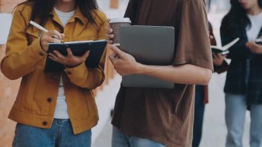 Kampüste elinde tablet bilgisayar ve not defteri olan bir grup öğrenci