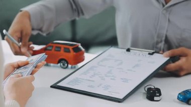 Arka planda araba modeli olan bir adam arabanın anahtarlarını tutuyor..