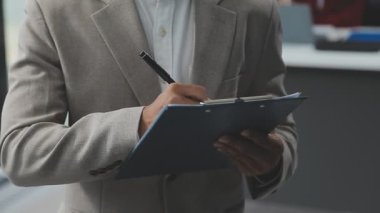 Genç erkek yönetici ofiste dururken deftere notlar yazıyor.