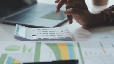 Genç işadamı masadaki mali hesapları analiz etmek için hesap makinesi kullanıyor..