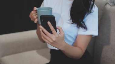 Güzel Asyalı kadın sabah kahveyle akıllı telefon kullanır..