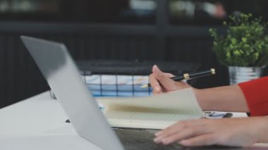 Kafede dizüstü bilgisayar ve defterle çalışan genç bir kadın.