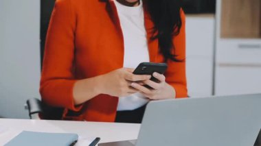 İş kadını ofiste dizüstü bilgisayarla çalışırken cep telefonu kullanıyor