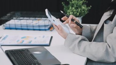 Genç iş kadını tablet bilgisayar kullanıyor ve ofisteki bir deftere yazı yazıyor.