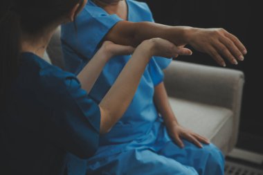 Evde dambıl kullanarak fizyoterapist eğitimi alan yaşlı bir kadın. Terapist, huzurevi egzersizlerinde yaşlı kadına yardım ediyor. Yaşlı bir hasta kollarını uzatmış halterler kullanıyor..