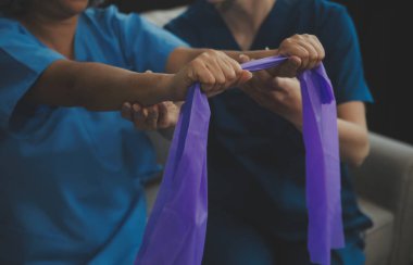 Özel antrenör, direniş bandında kıdemli bir kadına yardım ediyor. Rehabilitasyon fizyoterapi çalışanı huzurevindeki yaşlı hastaya yardım ediyor. Uzatma bandı olan yaşlı kadın fizyoterapist tarafından çalıştırılıyor..