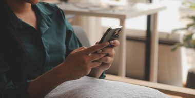 Çekici genç Asyalı kadın cep telefonu kullanıyor, internette iletişim kuruyor, çalışıyor ya da çevrimiçi öğreniyor, beyaz duvara karşı koltukta oturuyor, boş yer var. Güzel bir milenyum bayanı akıllı telefondan konuşuyor.