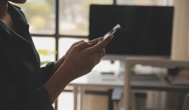 Ofiste telefonuyla gülümseyen bir iş kadını. Küçük işletme girişimcisi cep telefonuna bakıyor ve ofis arkadaşlarıyla konuşurken gülümsüyor.