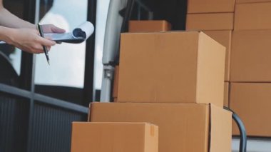 Elinde cep telefonu olan bir paket kutusu olan genç bir adam. Arkaplanda paket kutusu olan teslimatçı..