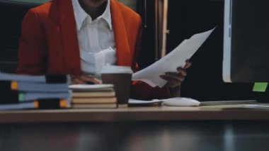 Takım elbiseli ve kravatlı işadamı ofiste otururken ellerinde belgeler tutuyor.