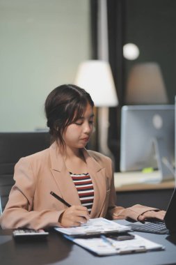 Telework konsepti - Asyalı iş kadını video toplantısına katılmak için dizüstü bilgisayar kullanır ve evdeki dijital tabletine notlar yazar