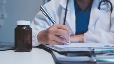 Kadın doktor masada deftere yazı yazıyor.