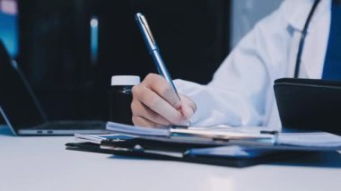 Beyaz önlüklü genç doktor masada oturuyor.