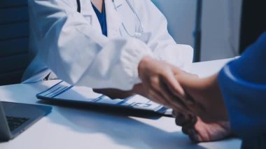 Kadın doktor elinde kalemle hastasına elini uzatıyor.