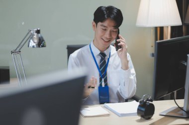 Kafede oturup telefonuyla konuşurken tablet bilgisayar kullanan beyaz gömlekli gülümseyen bir işadamı. Yana bak..