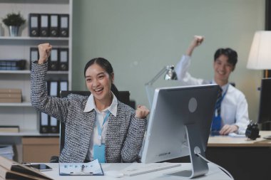 Cheerful businesspeople using a laptop in an office. Happy young entrepreneurs smiling while working together in a modern workspace. Two young businesspeople sitting together at a table.