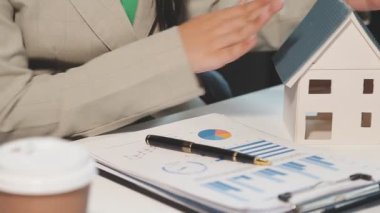 İşadamı masasında grafikle ev ve hesap makinesi tutuyor..