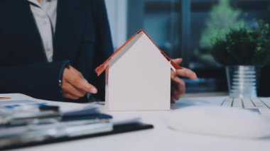 Ev modelini elinde tutan işadamı. Evin anahtarları masada.