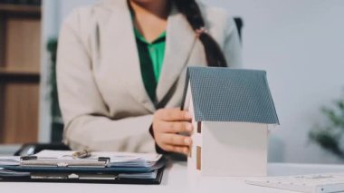 Takım elbiseli kadın model ev modelini elinde tutuyor.