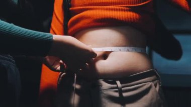 Genç bir kadın göbeğini mezurayla ölçüyor..