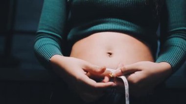 Karnında mezura olan bir kadın. Kız belini ellerinin arasında tutuyor..