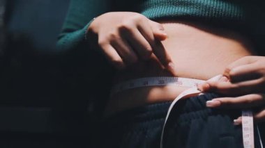 Karnını bantla ölçen bir kadın.