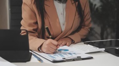 İş kadını ofisinde kalem ve defter yazıyor. Ofisteki bilgisayarda çalışıyor..