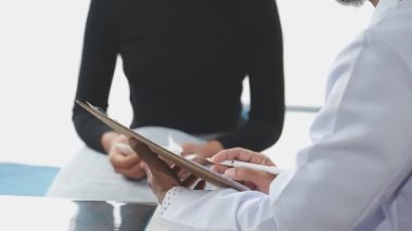 Kadın doktor klinikte dikilirken tablet tutuyor ve panoya yazı yazıyor..