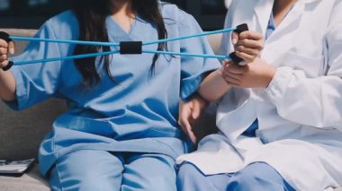 İki Asyalı doktor, bir tablet ve steteskoplu bir hastayı tartışıyorlar. Kanepede oturuyorlar ve tıbbi bir cihaz kullanıyorlar.