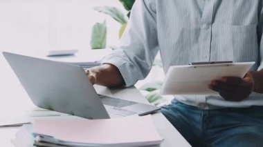 Genç işadamı dizüstü bilgisayarda çalışıyor ve ofiste tablet kullanıyor.