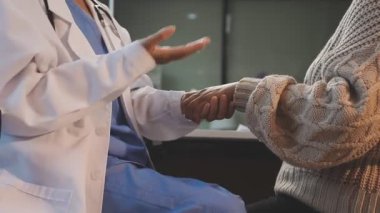 young doctor in medical uniform giving hand to female patient, closeup