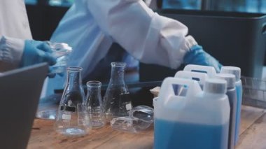Yakın plan bir bilim adamının laboratuarda cam şişeyle kimyasal bir sıvı tutarken görüntüsü..