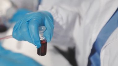 Eldivenli bir bilim adamı elinde pipetle elinde bir pipet tutuyor..