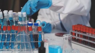 Mavi eldivenli laboratuvar asistanı kırmızı sıvıyı test tüpünde tutuyor..