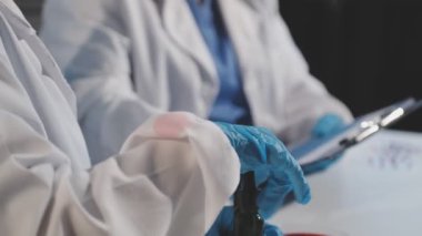 Koruyucu eldivenli bilim adamı elinde bir mikroskop tutuyor..